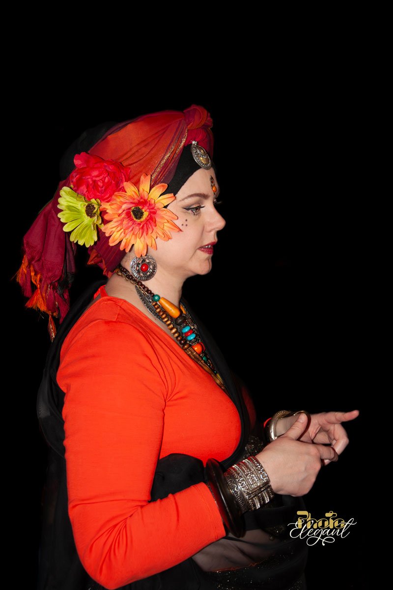 A young gypsy women in red traditional dresses with floral headscarves and silver jewelry on a black background